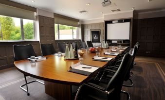 a large conference room with a wooden table , chairs , and a projector screen , set up for a meeting or presentation at Macdonald Berystede Hotel & Spa