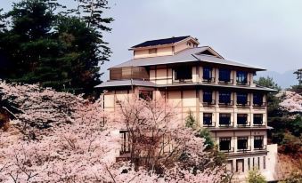 a large building with multiple floors is surrounded by trees and blooming cherry blossoms on a hillside at Jukeiso
