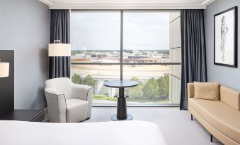 a modern hotel room with a large window offering a view of the city , a couch , and a chair at Sofitel London Gatwick