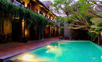 a pool is surrounded by a brick patio with tables and chairs , and several trees in the background at Rumah Batu Boutique Hotel