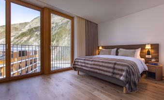 a large bedroom with a wooden floor and a bed next to a sliding glass door at Radisson Blu Hotel Reussen Andermatt