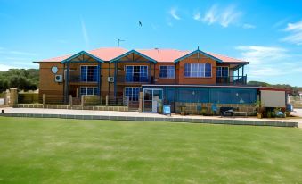a large wooden building with a red roof , surrounded by green grass and a clear blue sky at Seaspray Beach Holiday Park