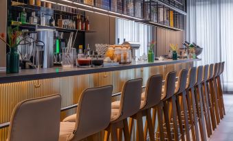 a modern bar with wooden chairs and shelves , featuring various drinks on the counter and a large window at Hilton Garden Inn Mannheim