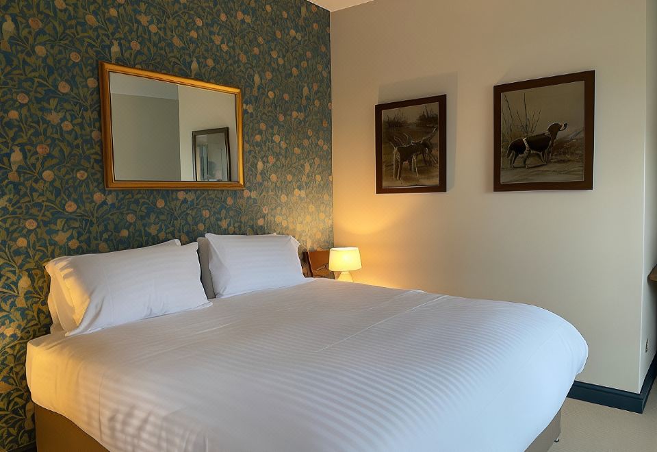 a large bed with white sheets and pillows is in a room with green floral wallpaper at The Seven Stars