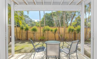 a patio area with a table and chairs , surrounded by palm trees and a fence at Hastings Cove Holiday Apartments