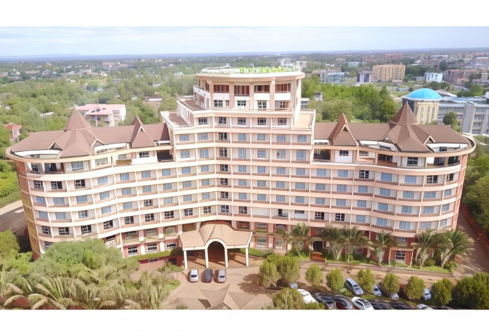 a large , multi - story building with a green roof and multiple balconies is surrounded by trees and parking lots at Rainbow Ruiru Resort