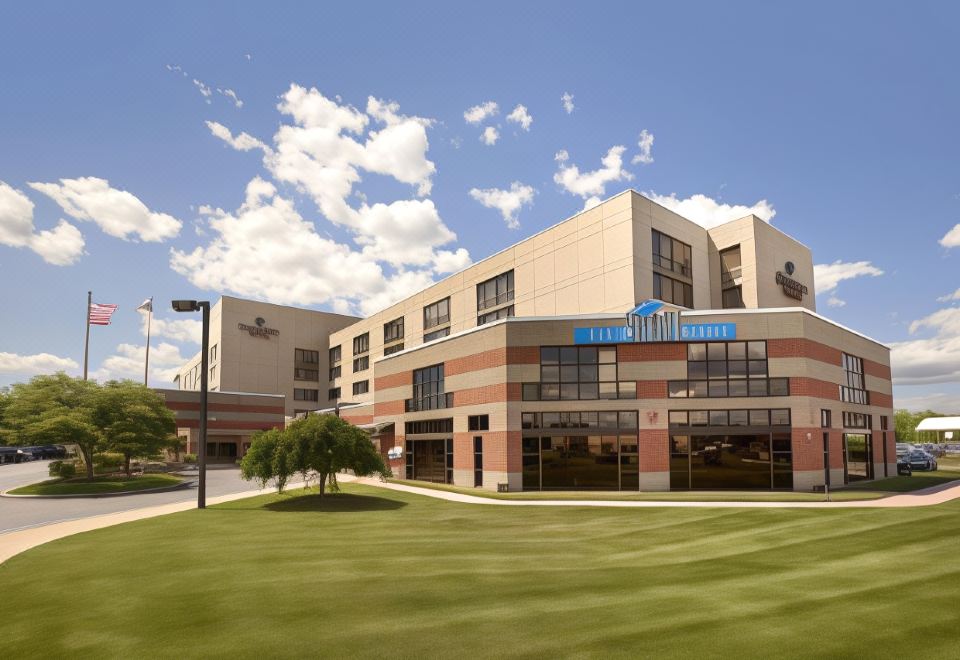 "a large building with a blue sign that says "" parikh executive suites "" is surrounded by a green lawn and trees" at DoubleTree by Hilton Hartford - Bradley Airport
