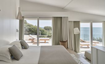a modern bedroom with large windows offering an ocean view , a bed , and white bedding at Falkensteiner Resort Capo Boi