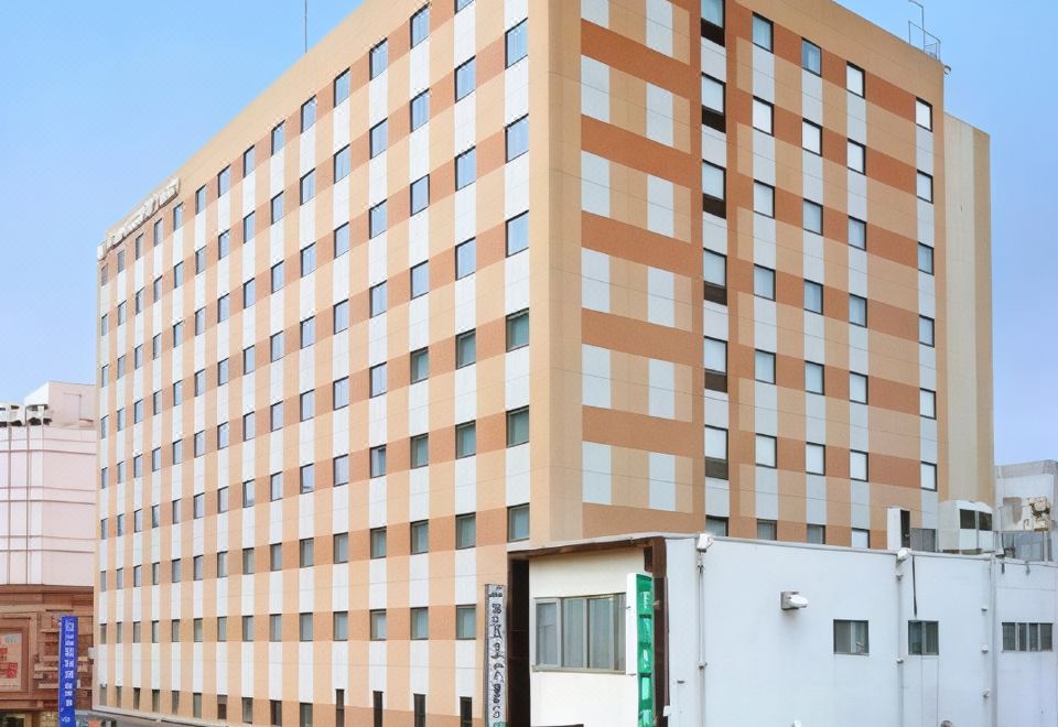 a tall , beige - colored building with multiple floors and white walls , situated on a busy city street at Daiwa Roynet Hotel Hachinohe