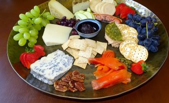 a round metal platter filled with a variety of fresh fruits , cheeses , and crackers on a dining table at Oyster Cove Chalet