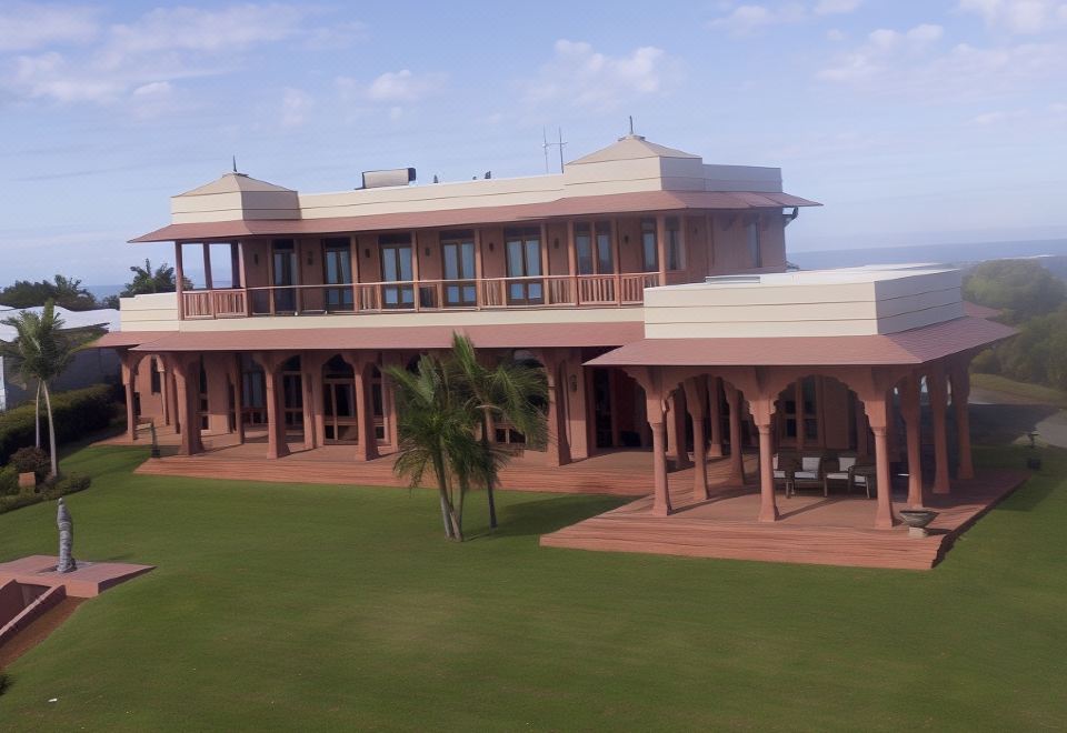 a large , two - story building with a red roof and balcony , surrounded by lush green grass and palm trees at Jodha Bai Retreat