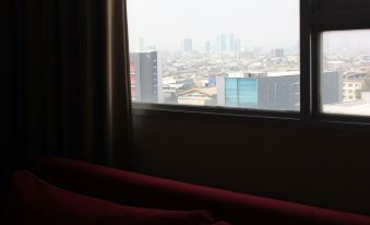 a view of a city through a window with a red couch in the foreground at ASTON Pluit Hotel & Residence