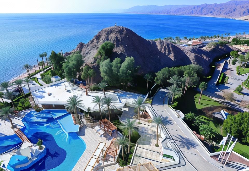 an aerial view of a luxurious resort with a pool surrounded by palm trees and mountains in the background at Steigenberger Hotel & Nelson Village, Taba
