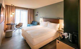 a large bed with white sheets is in a room with wooden floors and a window at Hilton Garden Inn Mannheim