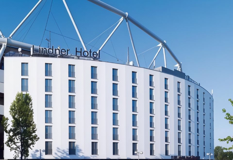 a large white hotel building with a blue and gray sign on top , situated in a city street at Lindner Hotel Leverkusen Bayarena