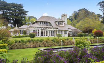 a large house with a gray roof is surrounded by a lush green lawn and purple flowers at Parklands Country Gardens & Lodges Blue Mountains