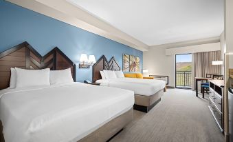a modern hotel room with two beds , white bedding , and a blue wall decorated with art at Camelback Lodge & Aquatopia Indoor Waterpark