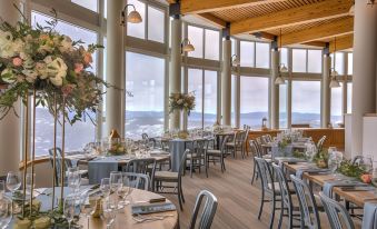 a restaurant with wooden tables and chairs , white tablecloths , and large windows overlooking the ocean at The Village at Palisades Tahoe