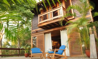 a wooden house surrounded by lush greenery , with a patio area featuring two blue chairs and a table at Aqua Nicaragua