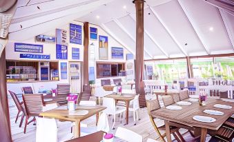 a large , open - air restaurant with white tables and chairs , surrounded by windows and blue posters on the walls at Le Life Resort