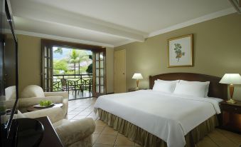 a large bedroom with a bed , chair , and sliding glass door leading to a balcony at Berjaya Beau Vallon Bay Resort & Casino