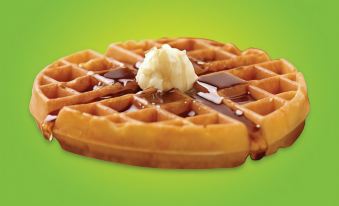 a green background with a waffle topped with whipped cream and chocolate sauce , placed on a dining table at La Quinta Inn & Suites by Wyndham Fairborn Wright-Patterson