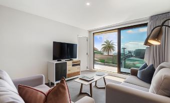 a living room with a large flat - screen tv mounted on the wall , a couch , and a dining table at Fernz Motel & Apartments Birkenhead