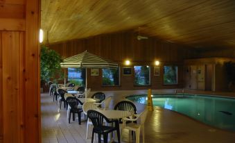 a pool area with wooden walls , tables and chairs , umbrellas , and potted plants , under a ceiling with exposed beams at Boarders Inn & Suites by Cobblestone Hotels - Superior/Duluth