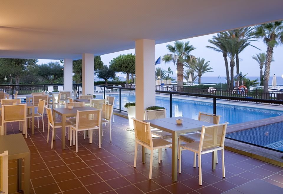 an outdoor dining area with white tables and chairs , surrounded by a pool and palm trees at Parador de Mojacar