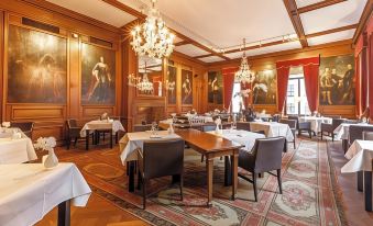 a large , elegant dining room with wooden walls , multiple tables , and chandeliers hanging from the ceiling at Fletcher Hotel Paleis Stadhouderlijk Hof