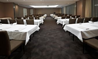 a large conference room with rows of tables and chairs , all covered in white tablecloths at Hotel 115