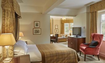 a hotel room with a king - sized bed , a flat - screen tv , and a dining table at Macdonald Berystede Hotel & Spa