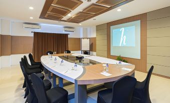 a modern conference room with a long wooden table , multiple chairs , and a large screen on the wall at Horison Tirta Sanita Spa Resort