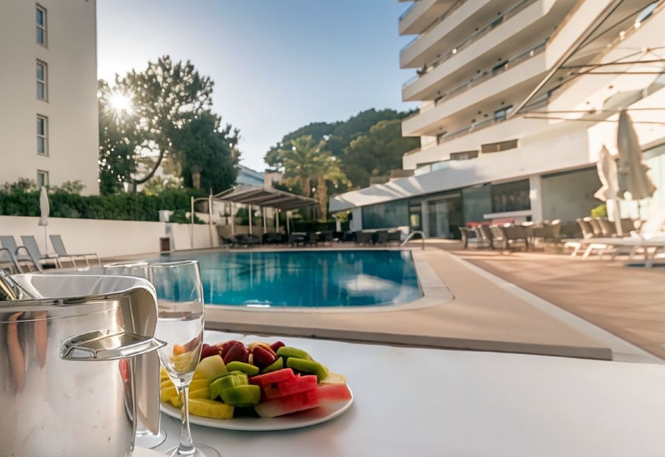 a table with a plate of fruit and a glass of water is set up near a pool in front of an apartment building at Hotel Principe Wellness&Spa