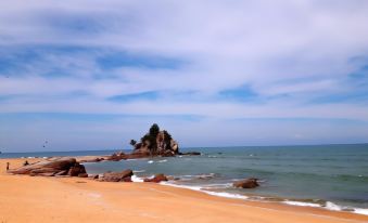 a sandy beach with a small island in the distance , surrounded by rocks and water at De' Chukai Hotel