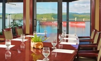 a dining room with a large table set for a meal , surrounded by chairs and a view of the water at Crest Hotel