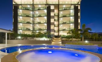 a large building with balconies and a swimming pool in front of it , lit up at night at Akama Resort