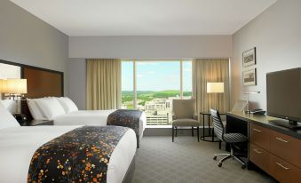 a hotel room with two beds , a desk , and a window overlooking a city view at DoubleTree by Hilton Cedar Rapids Convention Complex