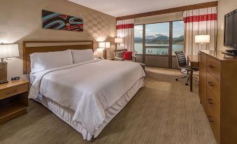 a large bed with white sheets and a wooden headboard is in the middle of a room with a view of water at Four Points by Sheraton Juneau