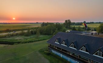 an aerial view of a building with a sunset in the background , surrounded by trees and grass at Van der Valk Hotel Volendam