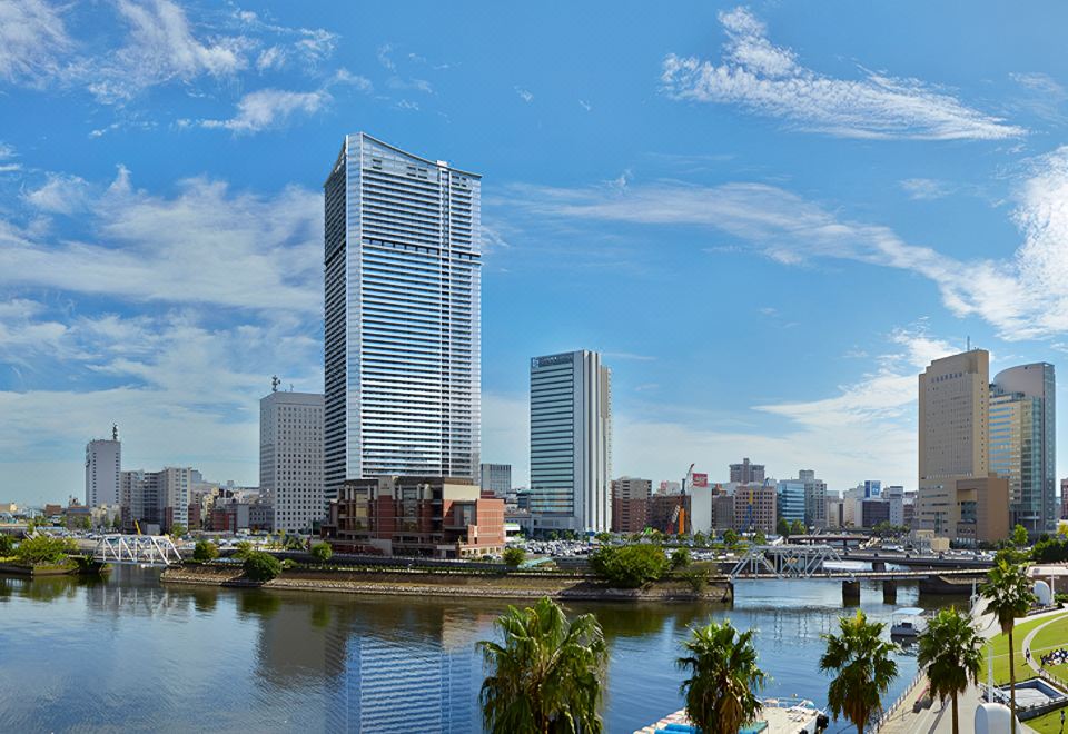a tall building with a large glass window is surrounded by palm trees and water at Oakwood Suites Yokohama
