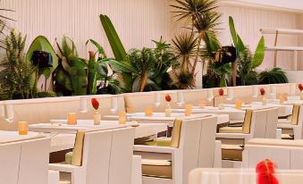 a modern dining room with white tables and chairs , set for a meal , surrounded by lush greenery at Cap d'Antibes Beach Hotel