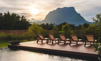 a serene outdoor setting with four lounge chairs and a swimming pool , surrounded by lush greenery and mountains in the background at Azalea Village