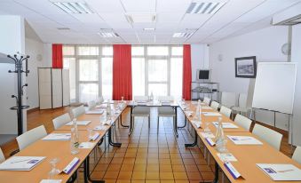 a conference room with long tables , chairs , and red curtains is set up for a meeting at Comfort Hotel Montlucon