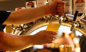 a man is pouring beer from a tap into a glass at a bar , surrounded by other people at The Marina Hotel - Mindarie