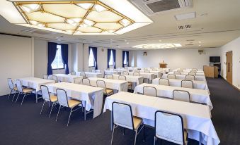a large conference room with multiple rows of tables and chairs , white tablecloths , and a large window at Airline Hotel