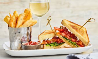 a plate of food , including a sandwich and fries , is displayed next to a glass of white wine at Courtyard Danbury