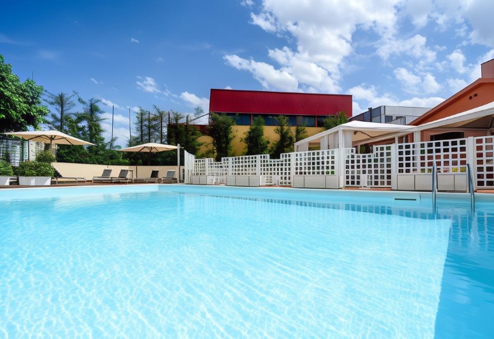 a large swimming pool with a red building in the background and white umbrellas around it at Hotel Concorde