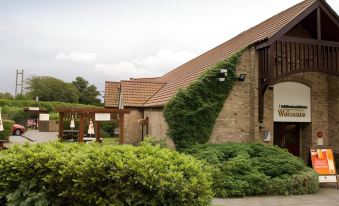 a brick building with a green ivy covered wall , surrounded by a lush garden and a wooden fence at Premier Inn Hull West