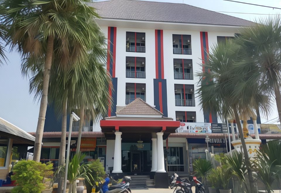 "a red and white building with a sign that says "" hotel "" is surrounded by palm trees" at Thanarom Place